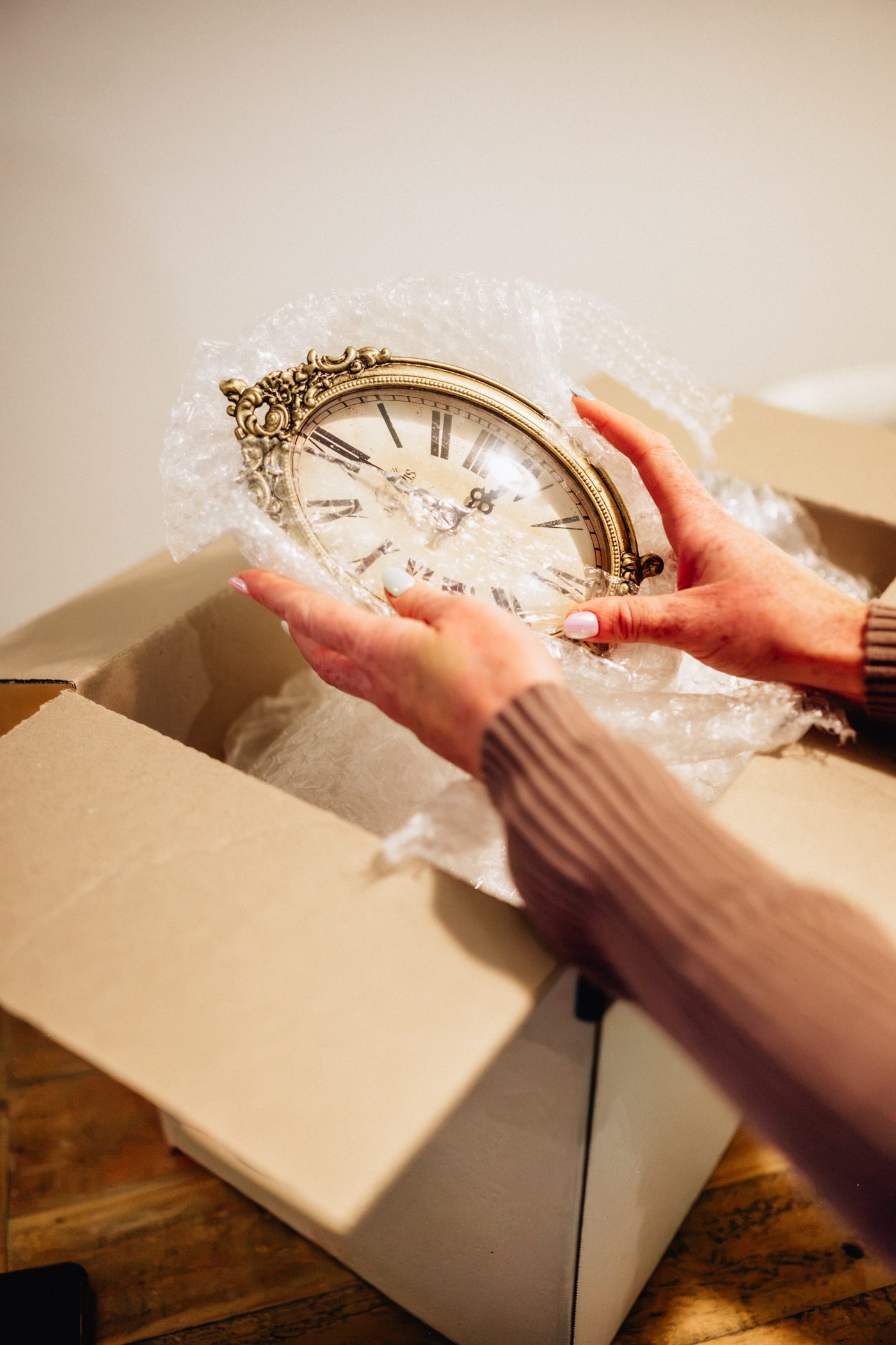Hands carefully wrapping an antique clock in bubble wrap to pack into a box