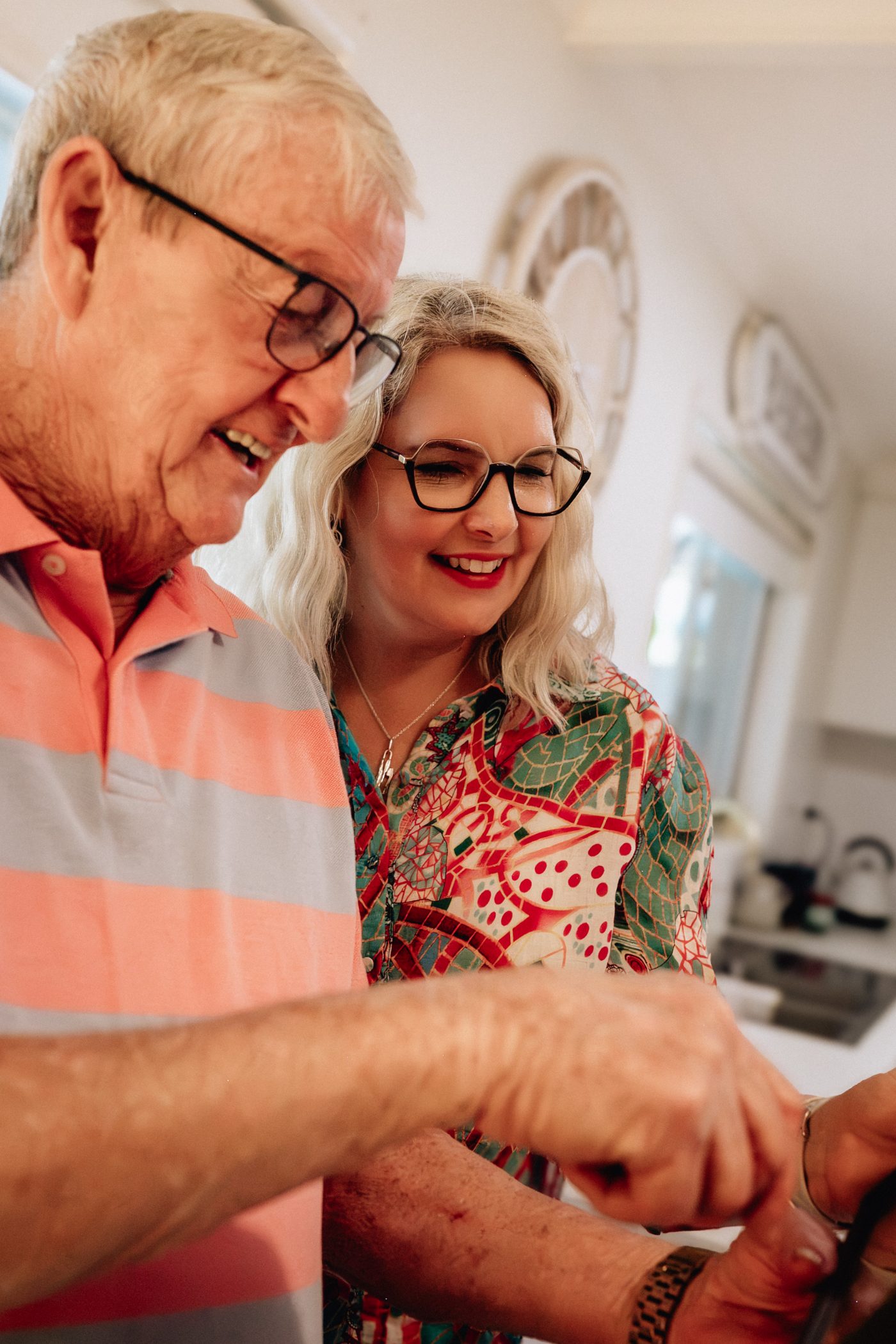 An older man and a smiling woman looking at something together in a bright kitchen